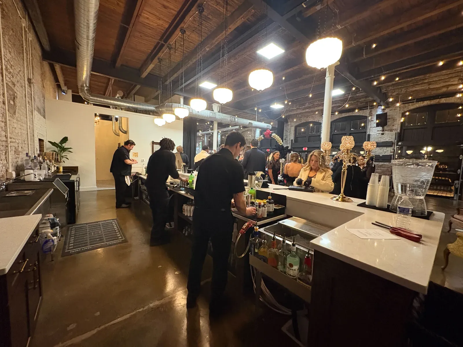 Bartenders serving guests at 24 Shelby's built-in bar with exposed brick and Edison string lights overhead