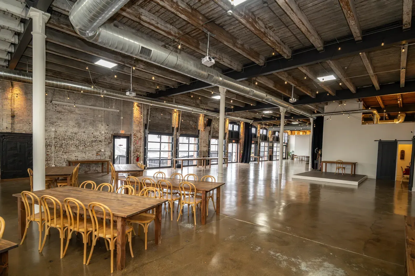 The Edison Room at 24 Shelby set with long farm tables and bentwood chairs facing the stage, the setup for a year-end awards show at a holiday party