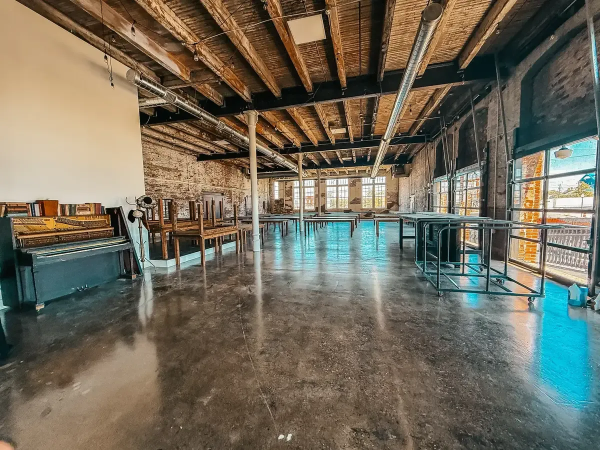 The Edison Room at 24 Shelby in its open setup, showing the original 1898 brick walls, exposed wood-beam ceilings, oversized windows, and Edison string lights — built-in venue character that decides whether a wedding venue is actually a value.
