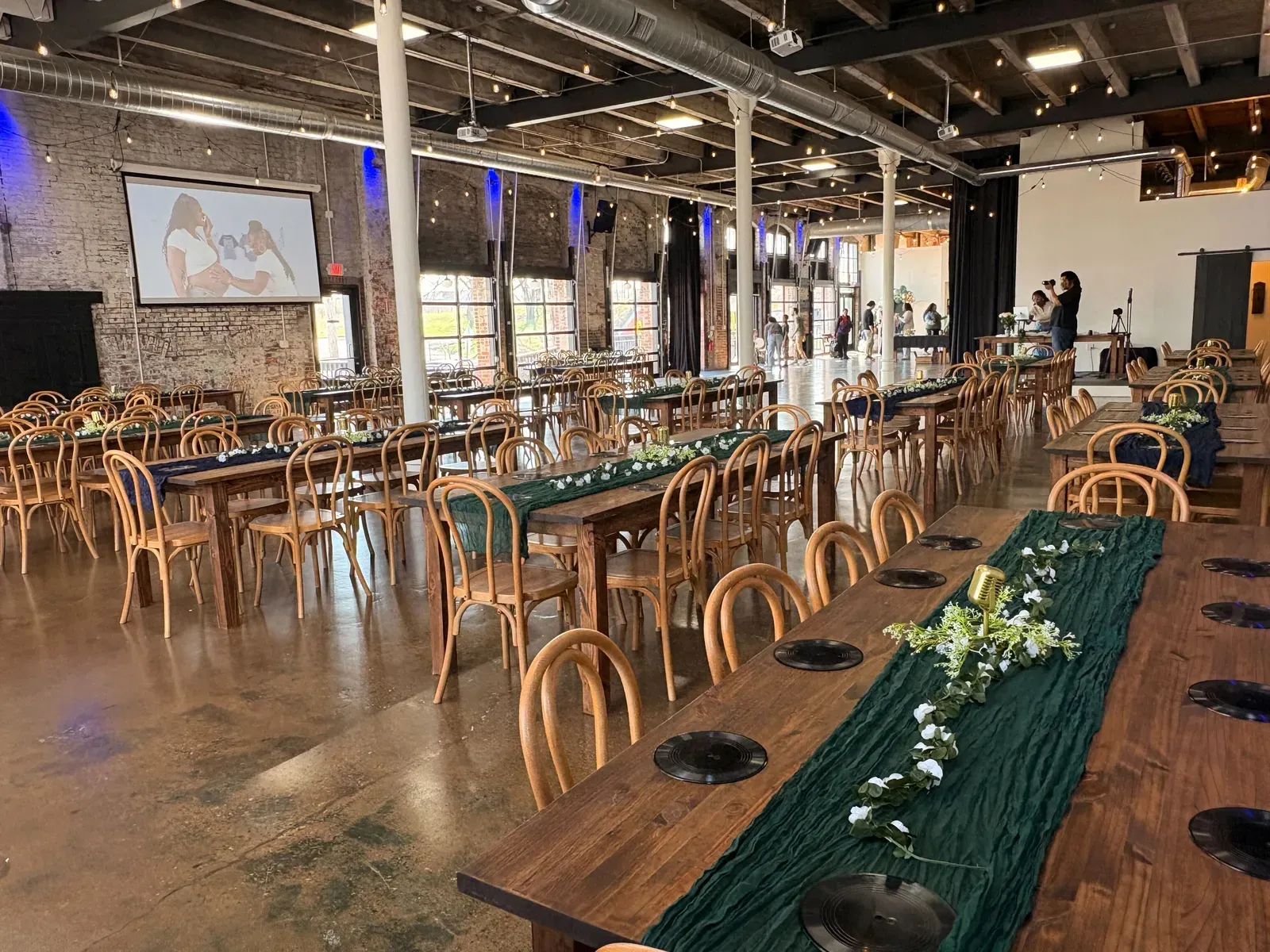 The Edison Room at 24 Shelby set up for an event, with original 1898 exposed brick walls, wood-beam ceilings, oversized windows, and Edison string lights overhead. The full indoor backup for any outdoor Indianapolis wedding venue plan.