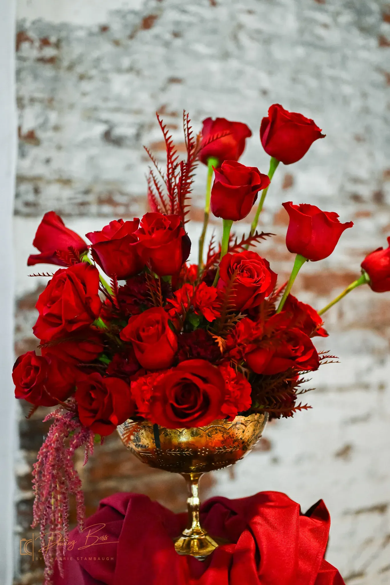Centerpiece detail with deep-red roses in a gold compote vase against 24 Shelby's exposed brick wall