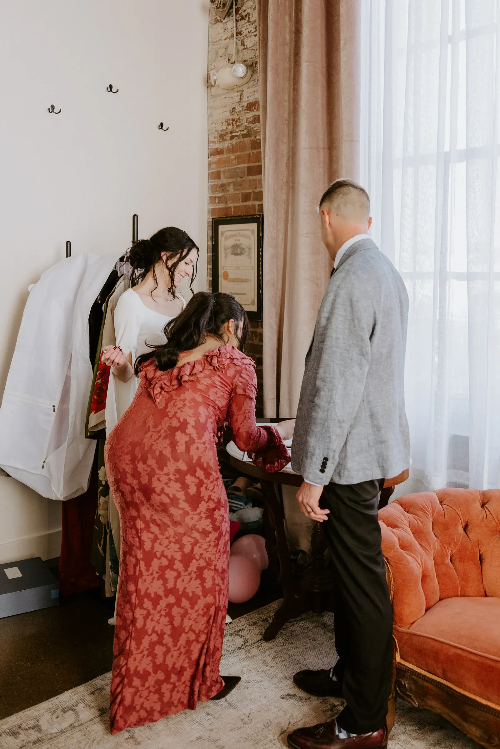 A small wedding party gathered for getting-ready preparations in an exposed-brick suite at 24 Shelby, dressed and laughing in soft window light, bridal robes still in the room