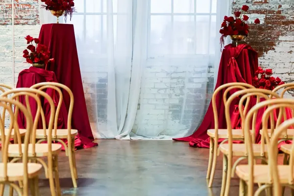 Indoor ceremony at 24 Shelby for an Indianapolis wedding in 2026, with rows of light wood chairs facing an altar of bold red drapery and oversized red and gold floral arrangements against original 1898 brick walls.