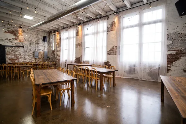 The Edison Room at 24 Shelby set with long farm tables and bentwood chairs under exposed 1898 brick and oversized windows, the room an outside caterer serves into at this Indianapolis wedding venue.