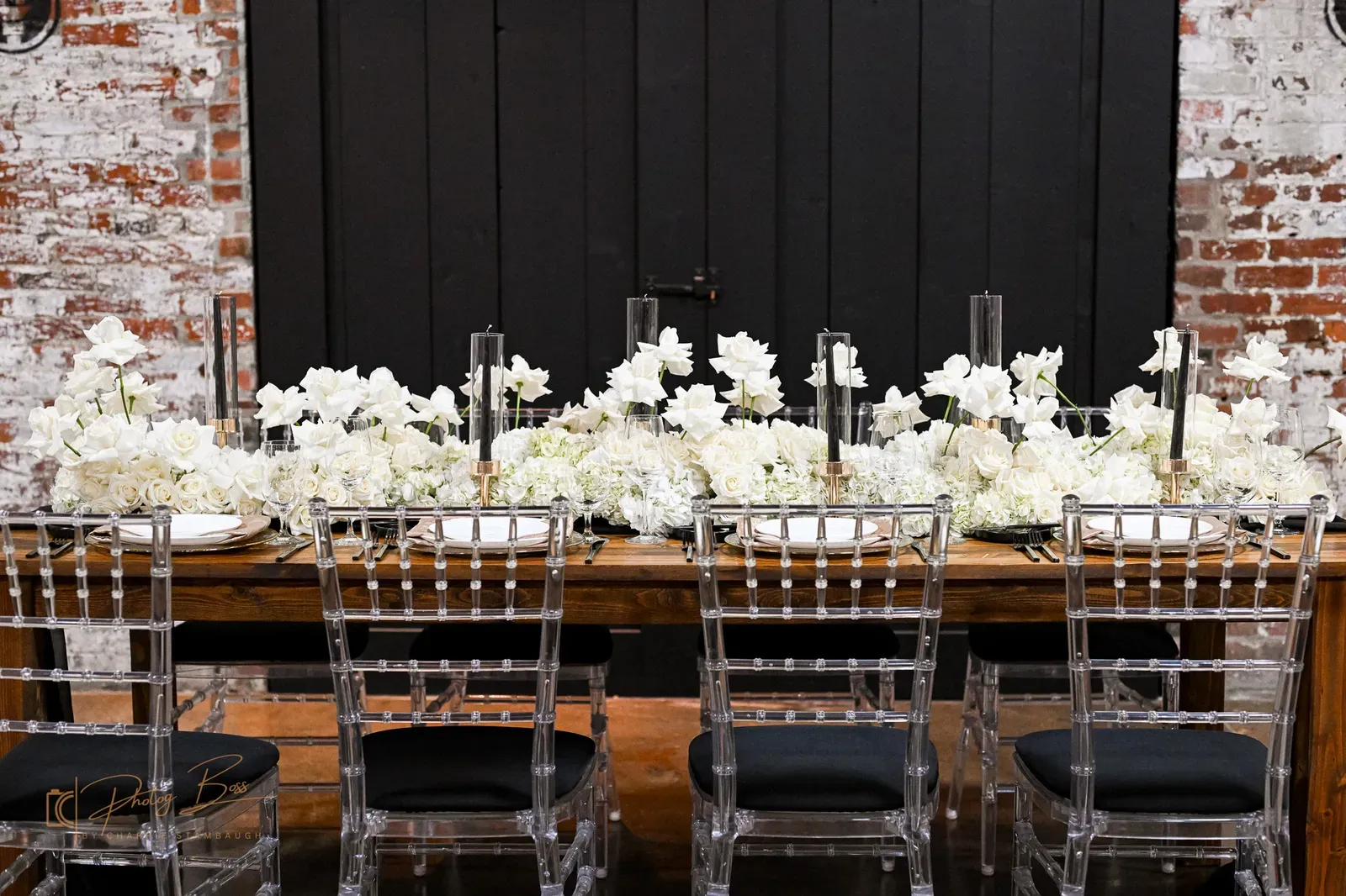 Wedding reception setup at 24 Shelby with farm tables, vintage chairs, candle centerpieces, original 1898 brick walls, and Edison string lights overhead. The Edison Room configured for a downtown Indianapolis wedding reception.