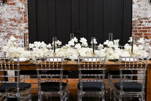 Wedding reception setup at 24 Shelby with farm tables, vintage chairs, candle centerpieces, original 1898 brick walls, and Edison string lights overhead. The Edison Room configured for a downtown Indianapolis wedding reception.