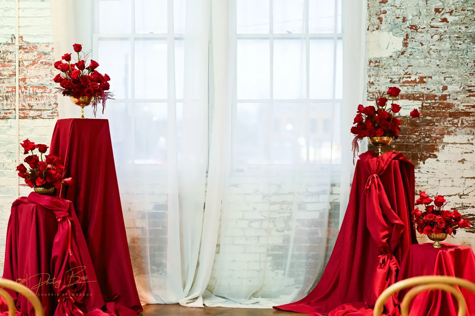 Bold red rose floral arrangements on draped wood tables at a 24 Shelby Indianapolis wedding with original brick walls and Edison string lights, illustrating the 2026 immersive design trend of sculptural drapery and elongated florals