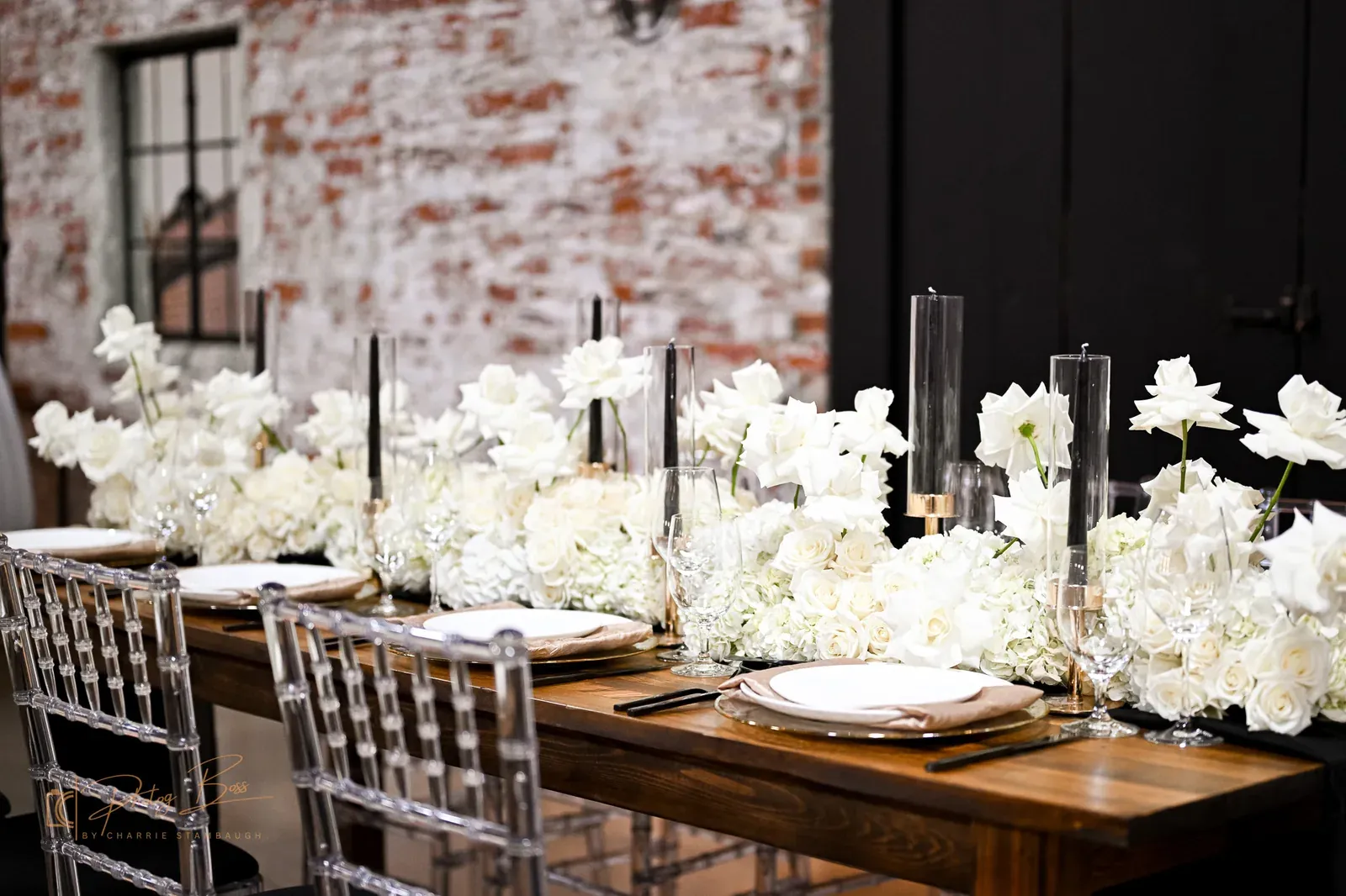 Long farm table set for an intimate Indianapolis wedding reception at 24 Shelby with white florals, black taper candles, and gold flatware against original 1898 brick walls, illustrating the 2026 trend toward smaller curated wedding environments