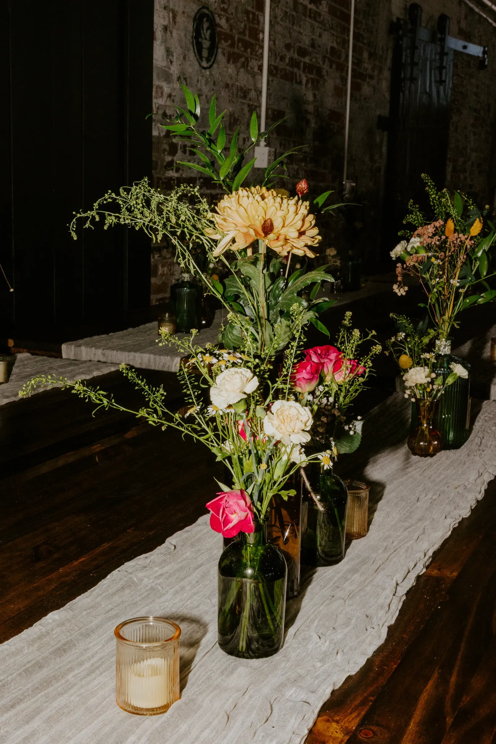 Long dark wooden reception table set for an intimate wedding dinner at an Indianapolis venue, vintage glassware, candle-low lighting, exposed brick walls in the background