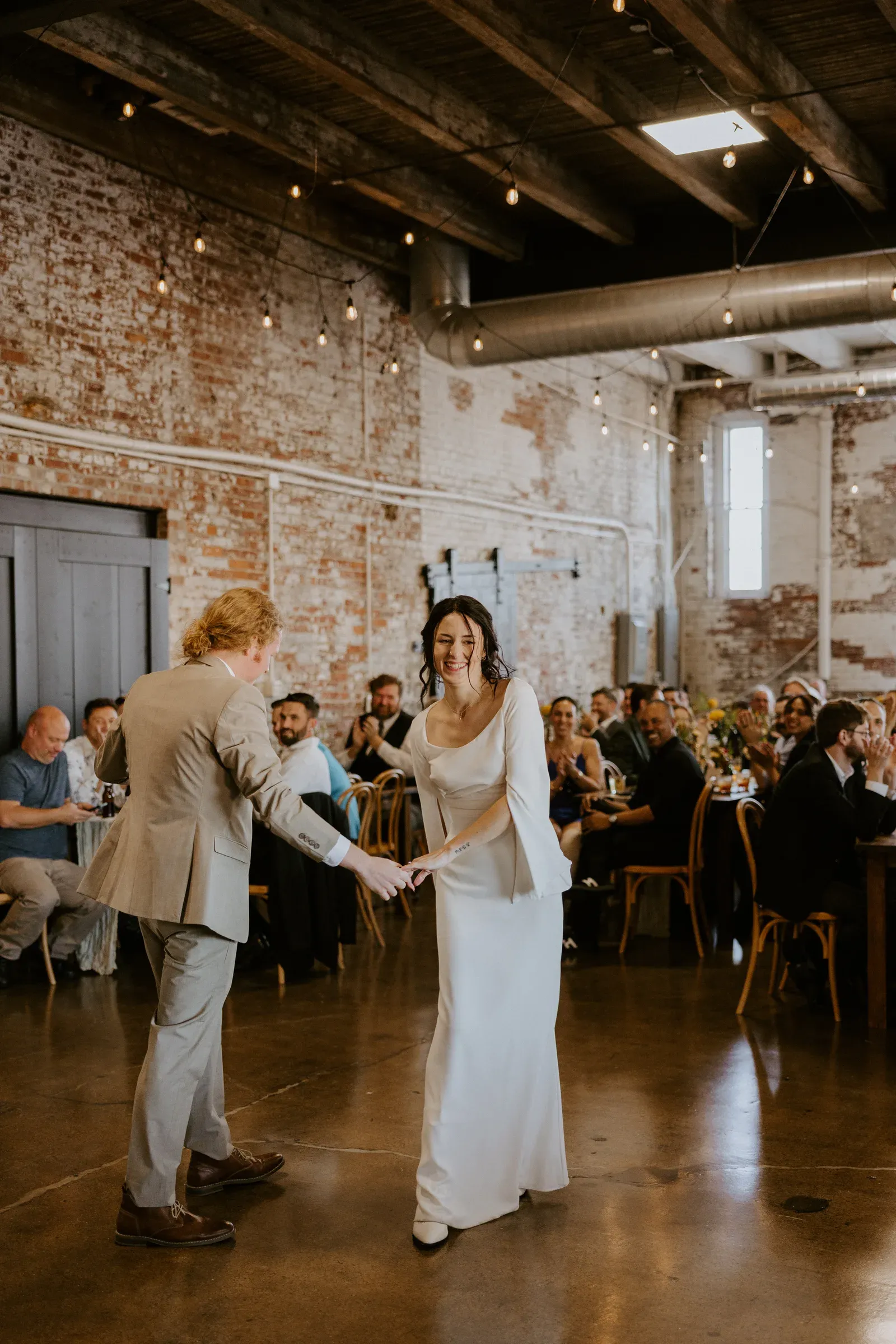 A first dance at a 24 Shelby wedding reception under Edison string lights with exposed 1898 brick walls in the background, the kind of day-of energy a thorough venue tour helps protect