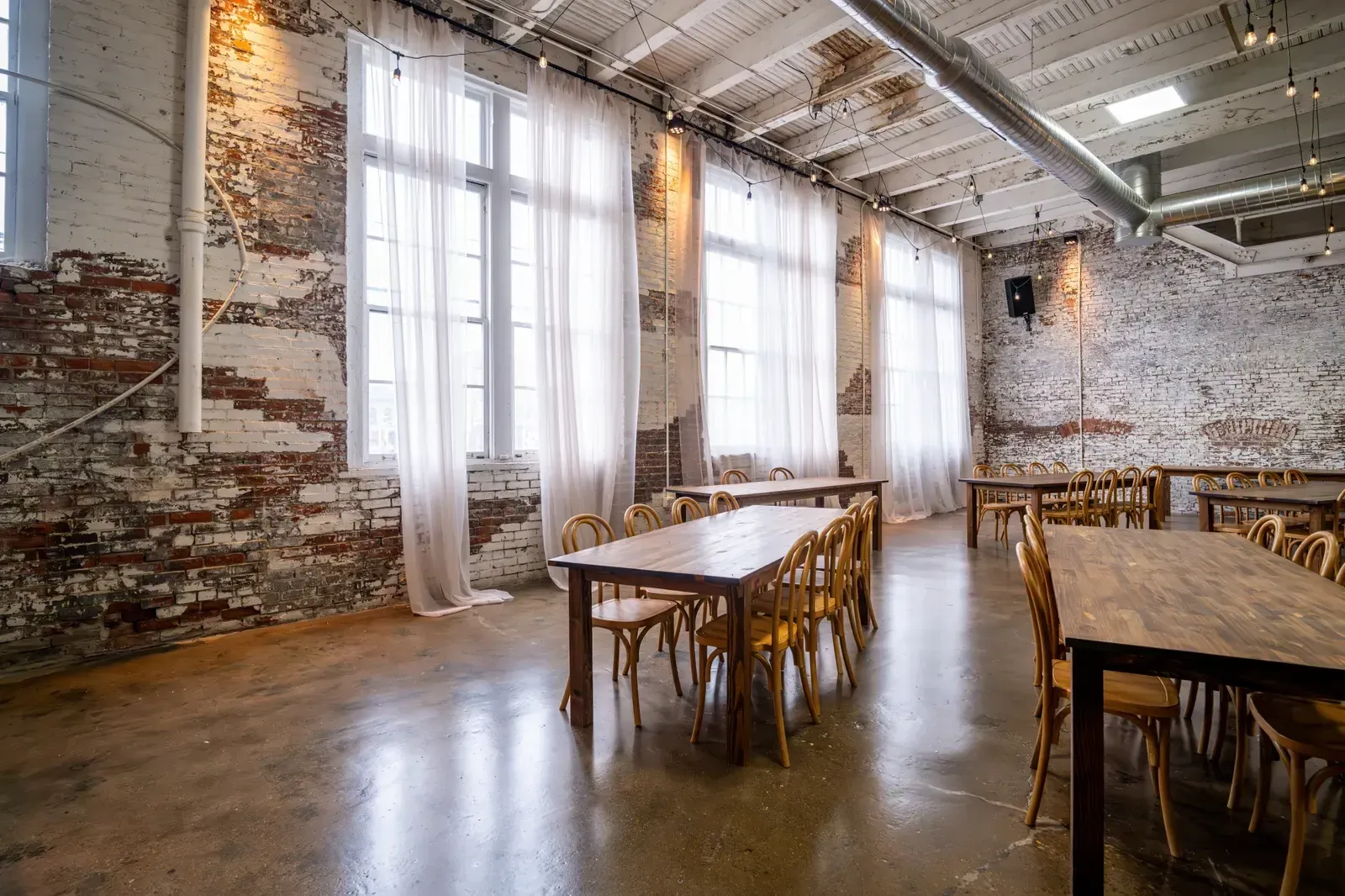 The Edison Room at 24 Shelby set for a seated dinner with farm tables and bentwood chairs, the space an outside caterer works into at an Indianapolis wedding venue that allows outside catering.