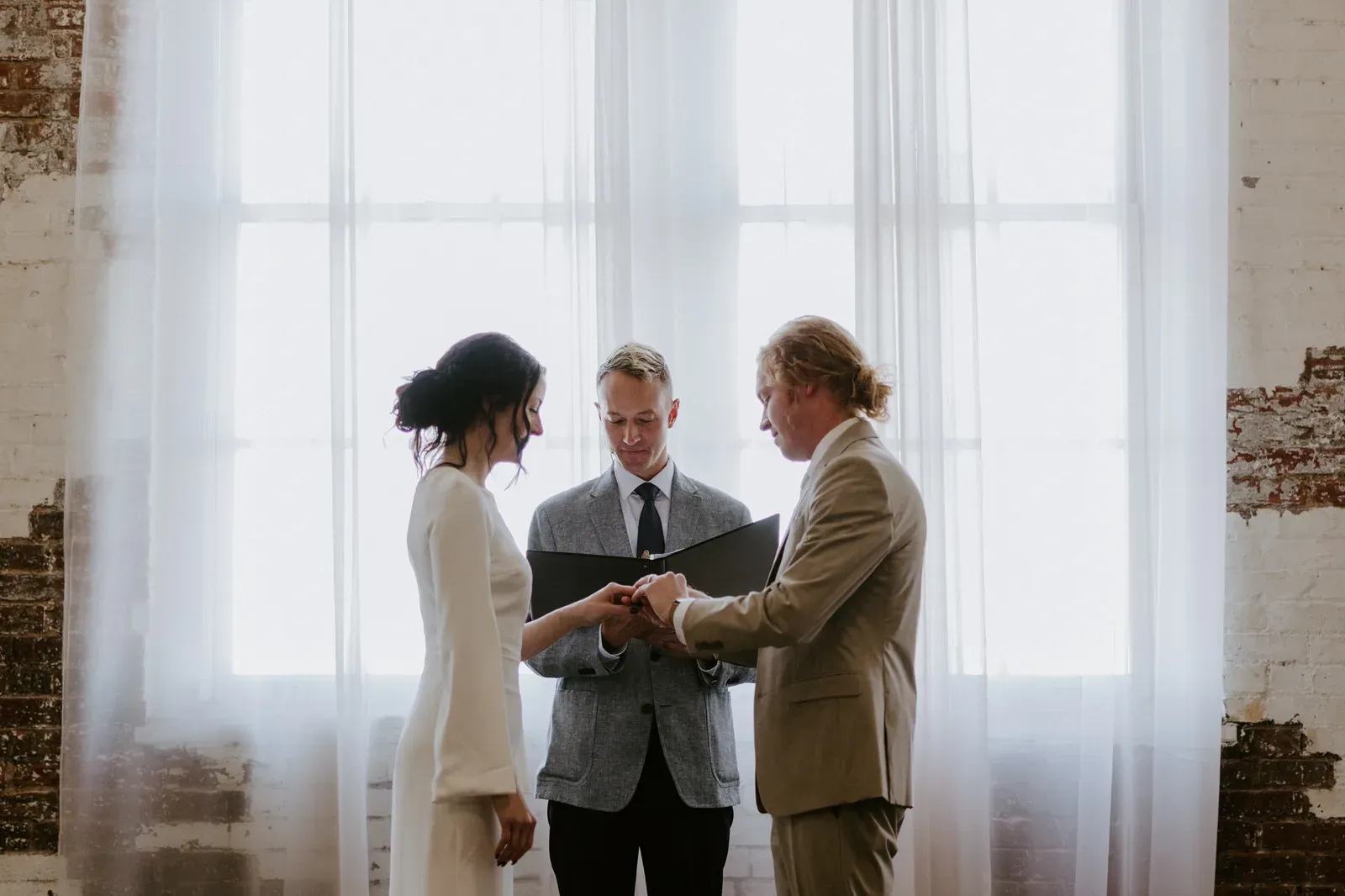 Indianapolis micro wedding ceremony moment at 24 Shelby with the couple exchanging vows in front of a small intimate group, framed by original 1898 brick walls and warm overhead lighting