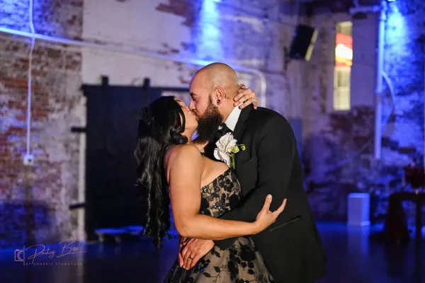 First dance at a 24 Shelby Indianapolis wedding under Edison string lights, with guests gathered at farm tables.