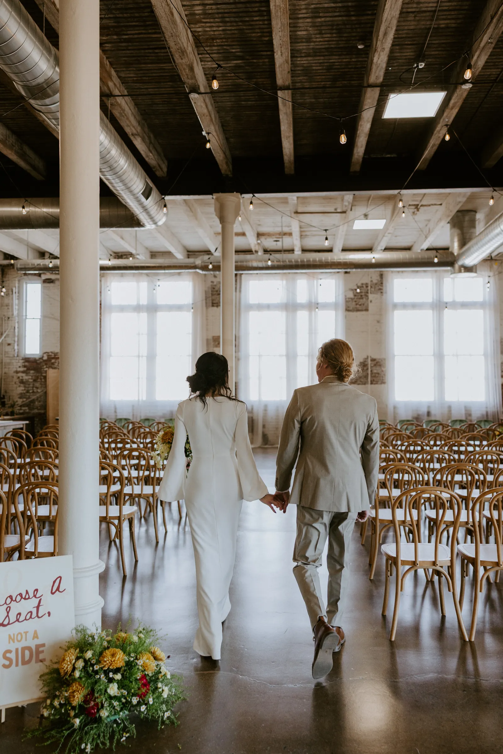 The Edison Room at 24 Shelby set up for a wedding ceremony — rows of chairs, exposed brick, Edison string lights